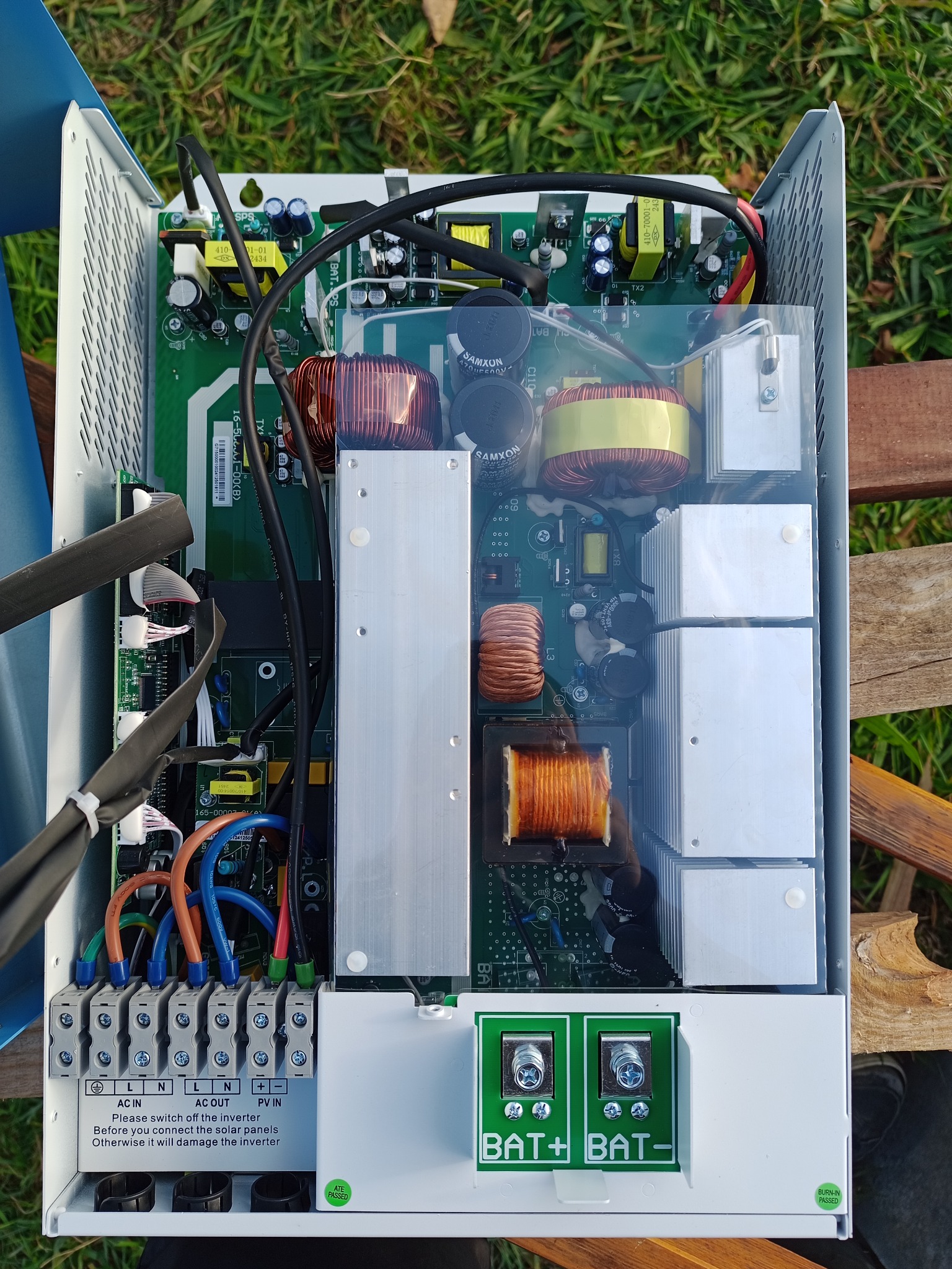 Otwarty falownik solarny Anenji po naprawie, widoczne wewnętrzne komponenty i przewody. Praca wykonana na zewnątrz, na drewnianym podłożu.