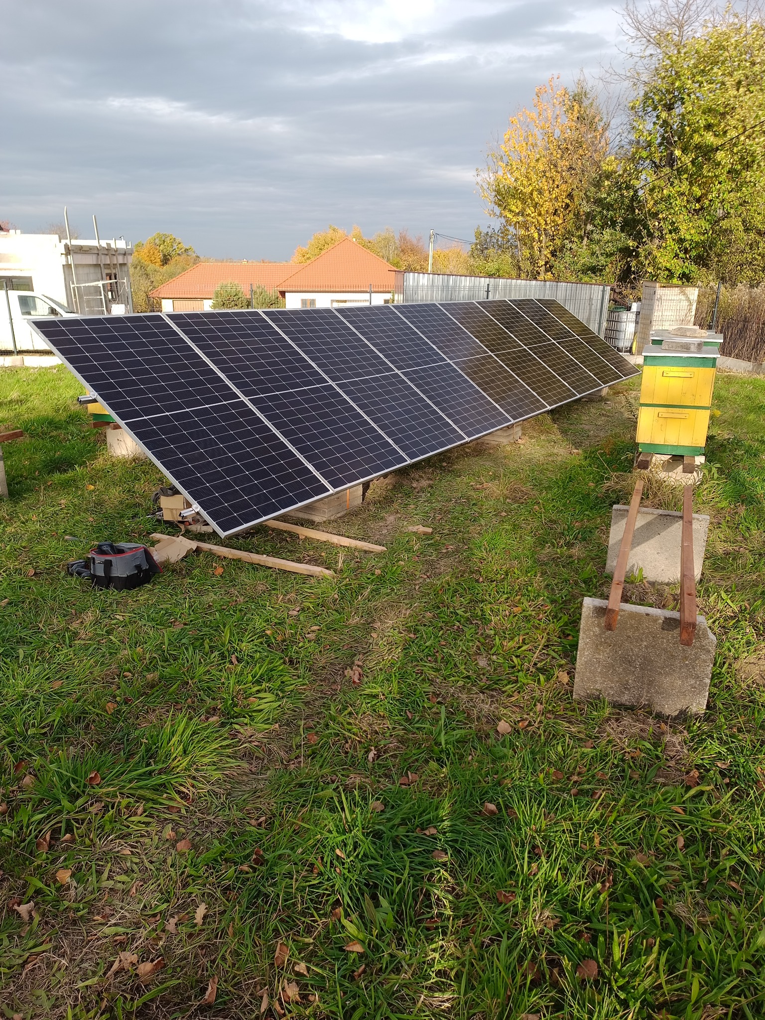 Panel fotowoltaiczny na gruncie, system balastowy, podłączony do falownika i magazynu energii. Zasilanie działki, widoczne ule w tle.