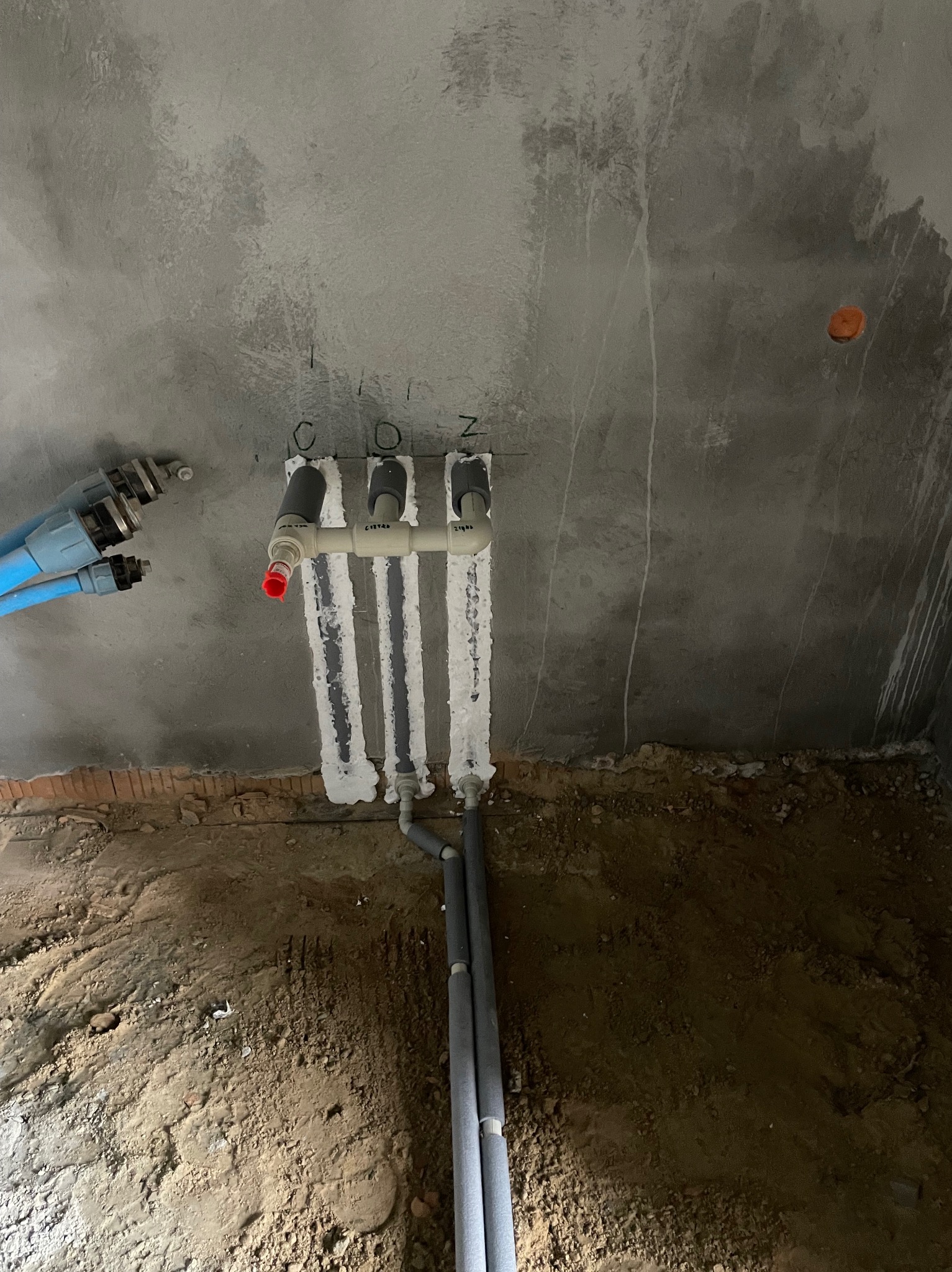 Surowy beton i rury instalacji COZ z izolacją, pionowo w ścianie. Część rur niebieskich. Widok z dołu na instalację w trakcie prac.