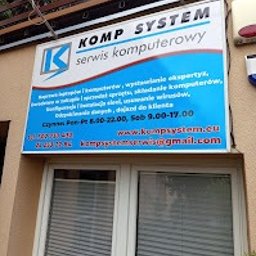 Komp System Marcin Siejak - Szyld reklamowy firmy KOMP SYSTEM z logo i zakresem usług (naprawa komputerów, instalacja sieci, odzyskiwanie danych) nad wejściem do biura z dwoma oknami.