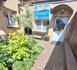 Wejście do firmy Komp System w Ząbkach. Widoczny szyld z logo, schludny chodnik z kostki i zadbana zieleń przed budynkiem.