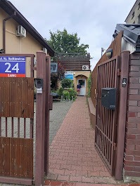 Wejście do biura firmy IT z ulicy, widoczne przez otwartą bramę. Tabliczka z adresem na budynku po lewej stronie. Osoba w drzwiach wejściowych.