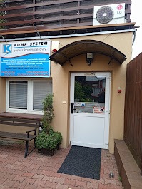 Wejście do serwisu komputerowego 'Komp System' z klimatyzacją LG, widoczne okno i ławka przed budynkiem. Ujęcie z poziomu chodnika.