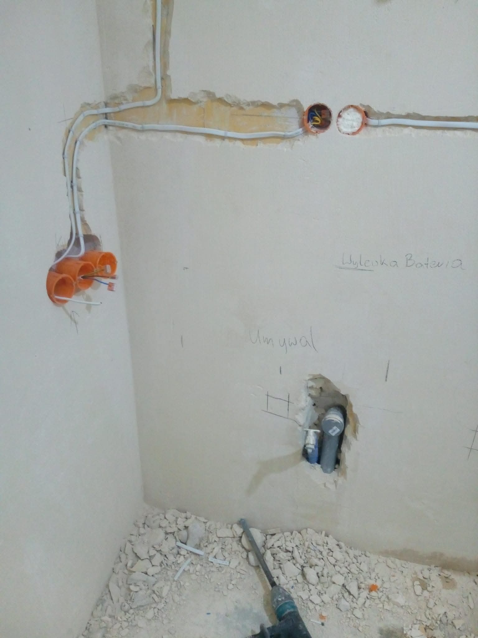 Instalacja elektryczna i hydrauliczna w trakcie remontu łazienki: kable w peszlach, puszki podtynkowe, rury odpływowe. Widoczne gruz i narzędzie.