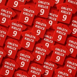 HexoCAD - Czerwone, gumowe zawieszki w kształcie koszulek z napisem 'Orlęta Kielce' i numerem 9, ułożone blisko siebie na czerwonym tle. Widok z góry, równomierne oświetlenie.