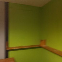 ADRIAN ZIELIŃSKI - Fragment wnętrza z zieloną ścianą i drewnianą półką. Nierównomierne oświetlenie, rozmycie. Widoczny fragment mebla w dolnej części kadru.