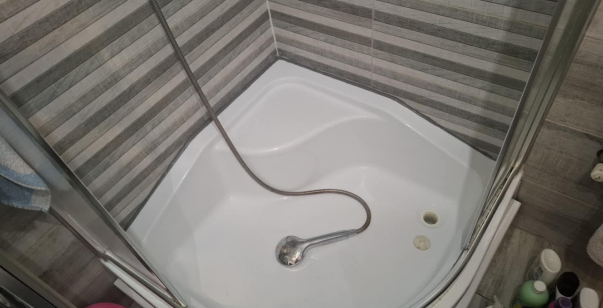 Wykończona kabina prysznicowa z szarymi płytkami imitującymi drewno na ścianach. Widoczna słuchawka prysznicowa i odpływ. Ukończony remont łazienki.