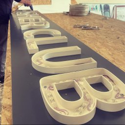 Region Projekt Weronika Galewska - Montaż podświetlanych liter przestrzennych na płycie. Widoczne diody LED wewnątrz liter i narzędzia pracy. Etap produkcji szyldu reklamowego.