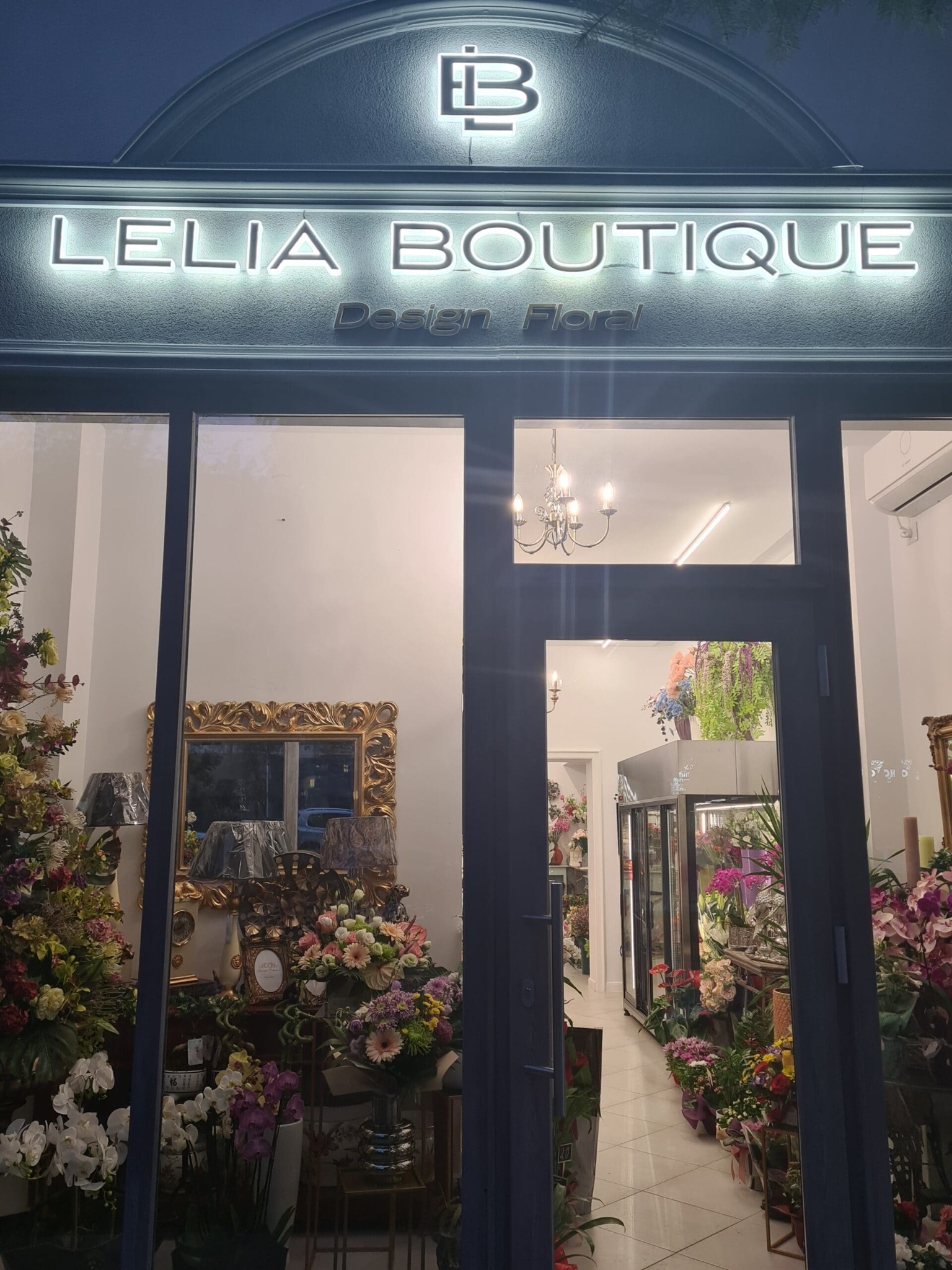 Elegancka witryna kwiaciarni 'Lelia Boutique Design Floral' z bogatą ekspozycją kwiatów i dekoracji, widoczna przez duże okna. Nad wejściem podświetlany szyld z logo.