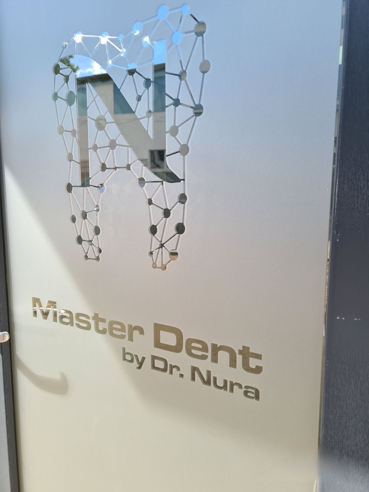 Oklejona szyba z logo dentystycznym 'Master Dent by Dr. Nura', przedstawiającym ząb z motywem sieci neuronowej. Minimalistyczny design w odcieniach szarości.