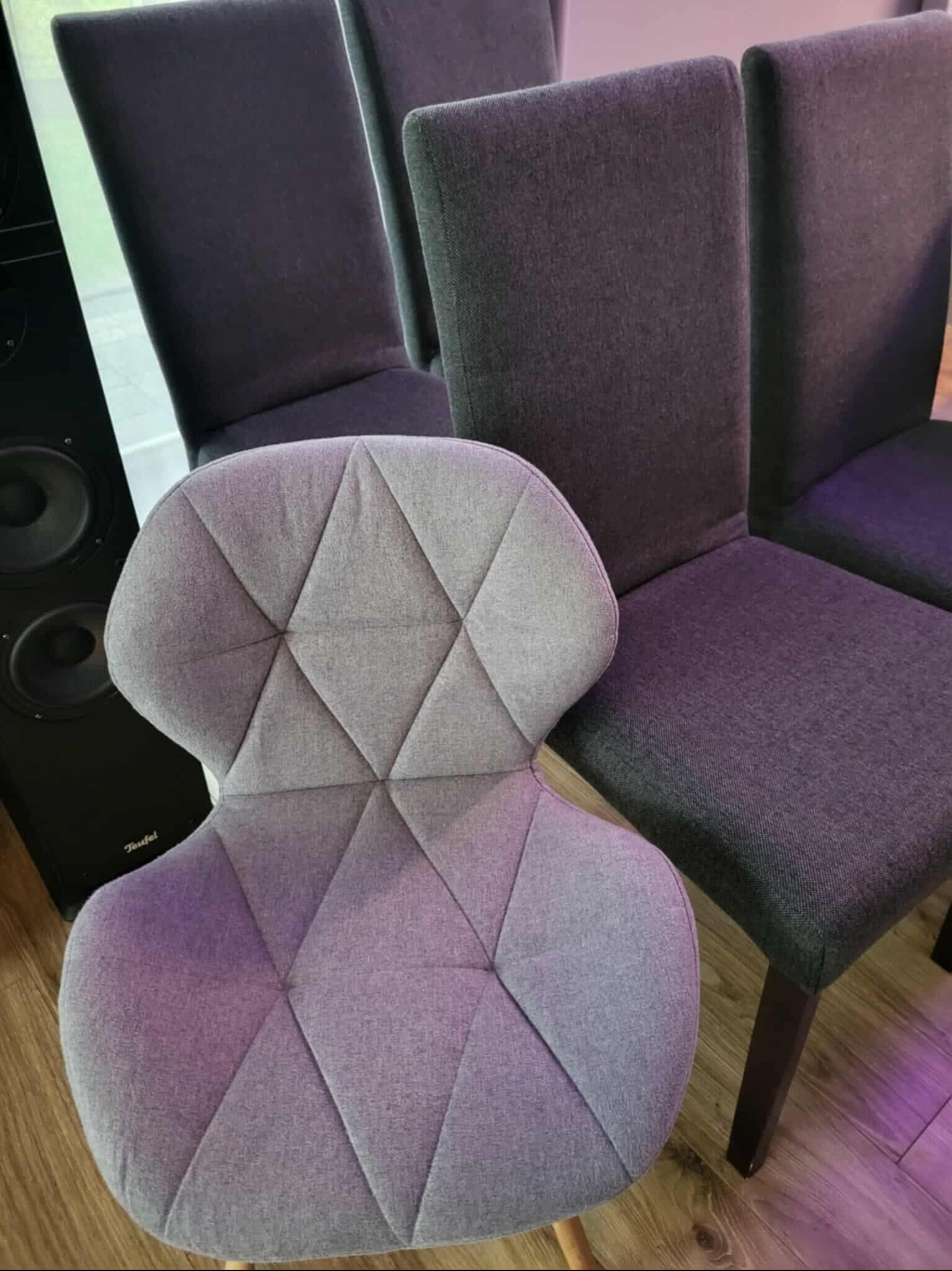 Szare krzesła tapicerowane, w tym jedno z geometrycznym wzorem, stojące na drewnianej podłodze obok czarnego głośnika. Widok z góry, bliski kadr.