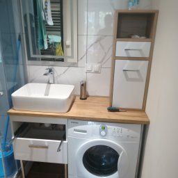 Sowbud Cezary Sowiński - Nowoczesna łazienka z pralką zabudowaną pod blatem z umywalką, szafką wiszącą i lustrem. Biało-szara kolorystyka, widoczny otwarty szuflada i narzędzie na blacie.