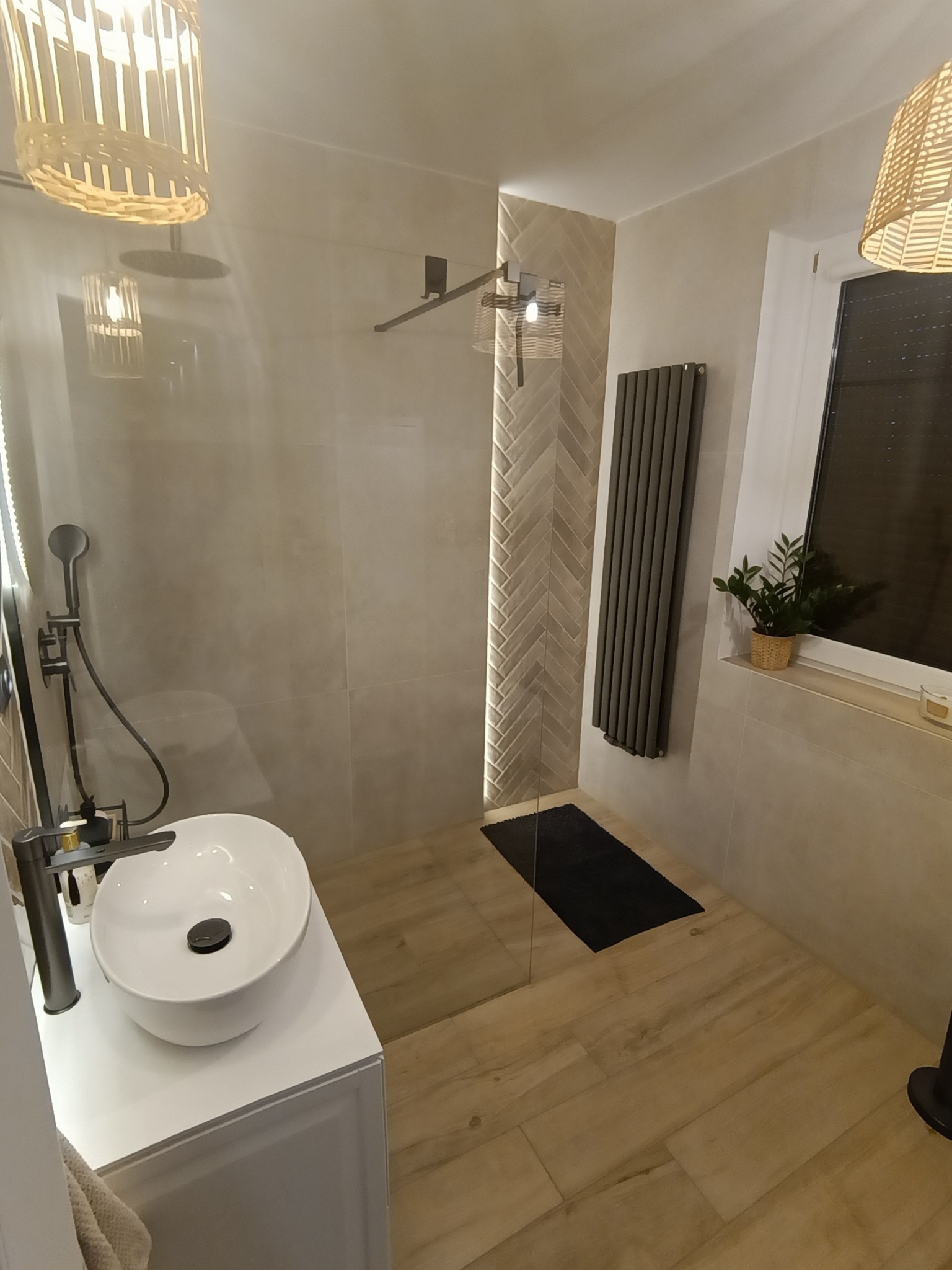 Nowoczesna łazienka z kabiną prysznicową typu walk-in, umywalką nablatową i grzejnikiem drabinkowym. Płytki imitujące drewno na podłodze i ścianie w strefie prysznica.