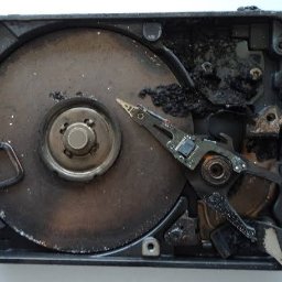 iTechData - Odzyskiwanie danych Kraków - Uszkodzony dysk twardy po awarii, widoczne ślady przepalenia i uszkodzenia mechaniczne. Głowica odczytująca nad talerzem. Czarna obudowa.