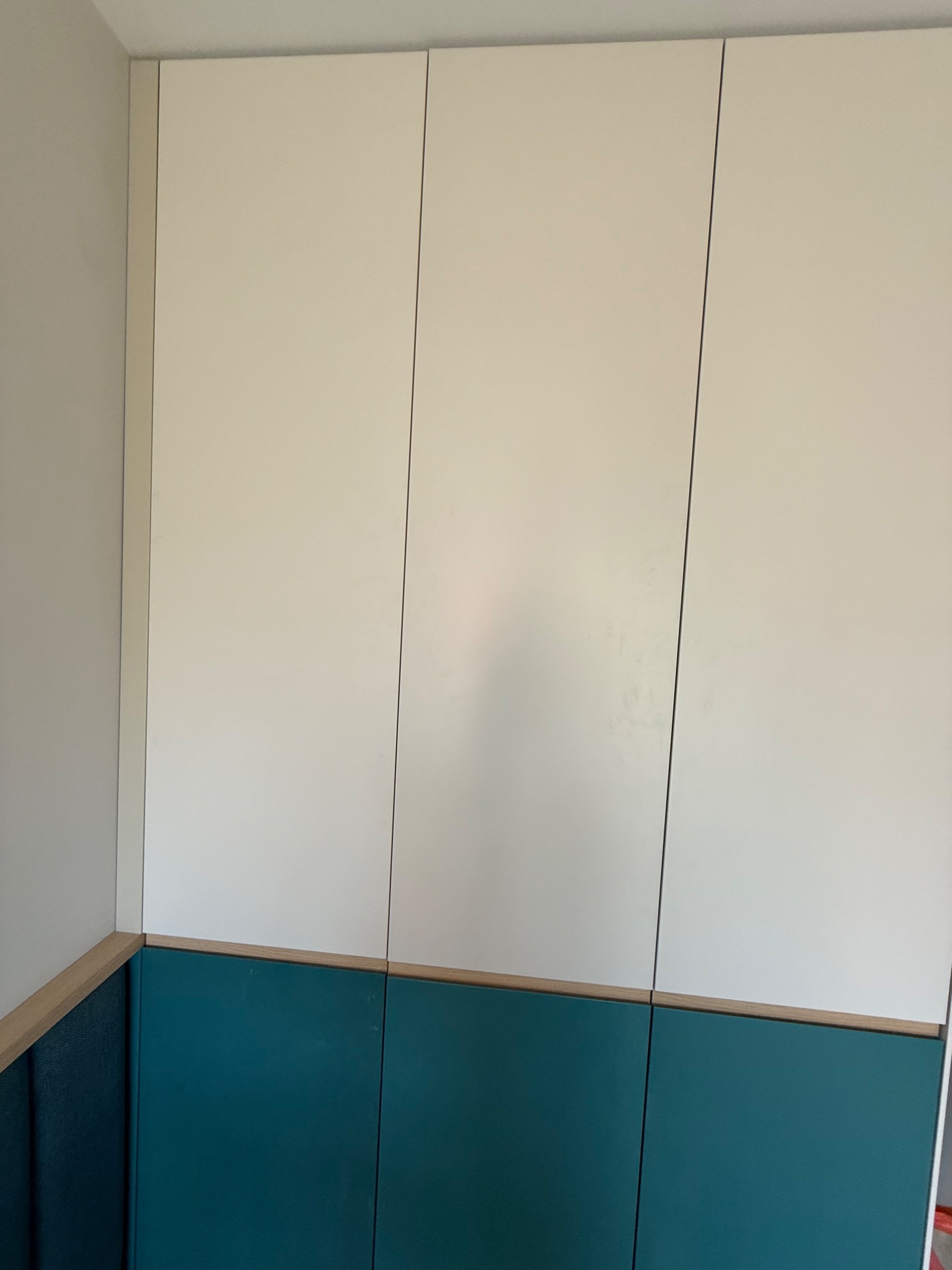 Biało-turkusowa szafa wnękowa z drewnianymi akcentami, wykonana na wymiar w Kartuzach. Minimalistyczny design, gładkie fronty, brak uchwytów.