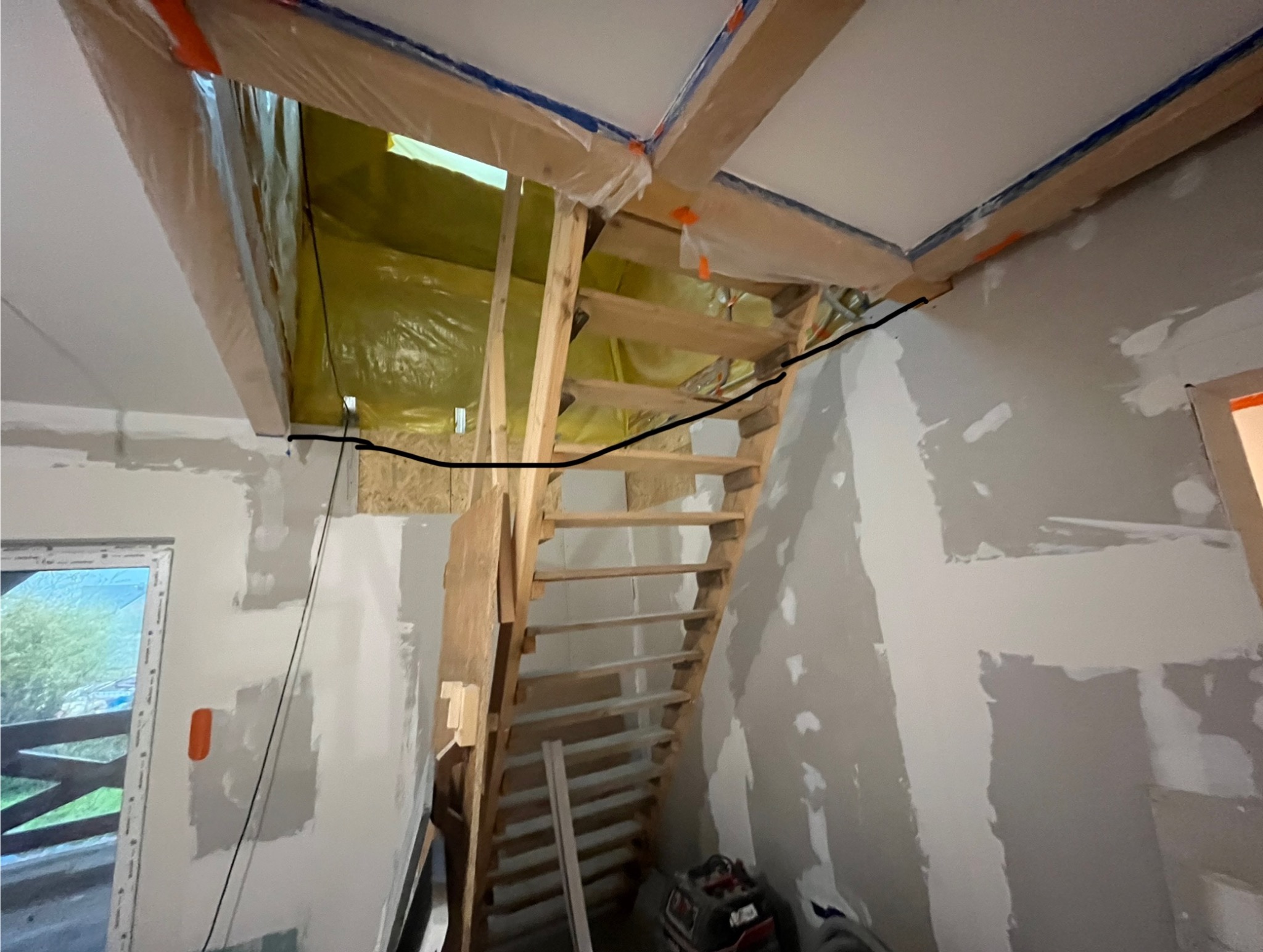 Wnętrze w trakcie remontu: drewniane schody na poddasze, ściany w szpachli, zabezpieczone folią elementy konstrukcyjne sufitu. Widoczne narzędzia.