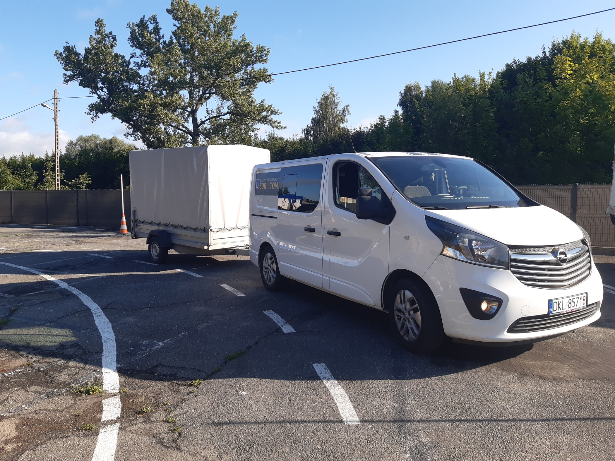 Biały bus Opel Vivaro z przyczepą na placu manewrowym, widoczny napis 'Rejestracja nauka jazdy EUR-TOM'.
