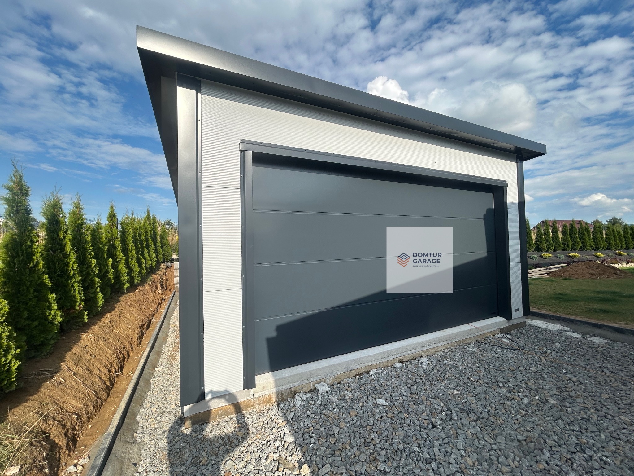 Nowoczesny garaż blaszany z bramą segmentową, wykonany z płyty warstwowej PIR 100 mm z ukrytym łącznikiem. Widoczna podkonstrukcja pod panele fotowoltaiczne.