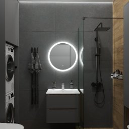 Kiryl Stepaniuk DS Studio - Nowoczesna łazienka z szarą armaturą, okrągłym lustrem z podświetleniem LED, drewnianą podłogą i kabiną prysznicową typu walk-in. Pralka i suszarka w zabudowie.