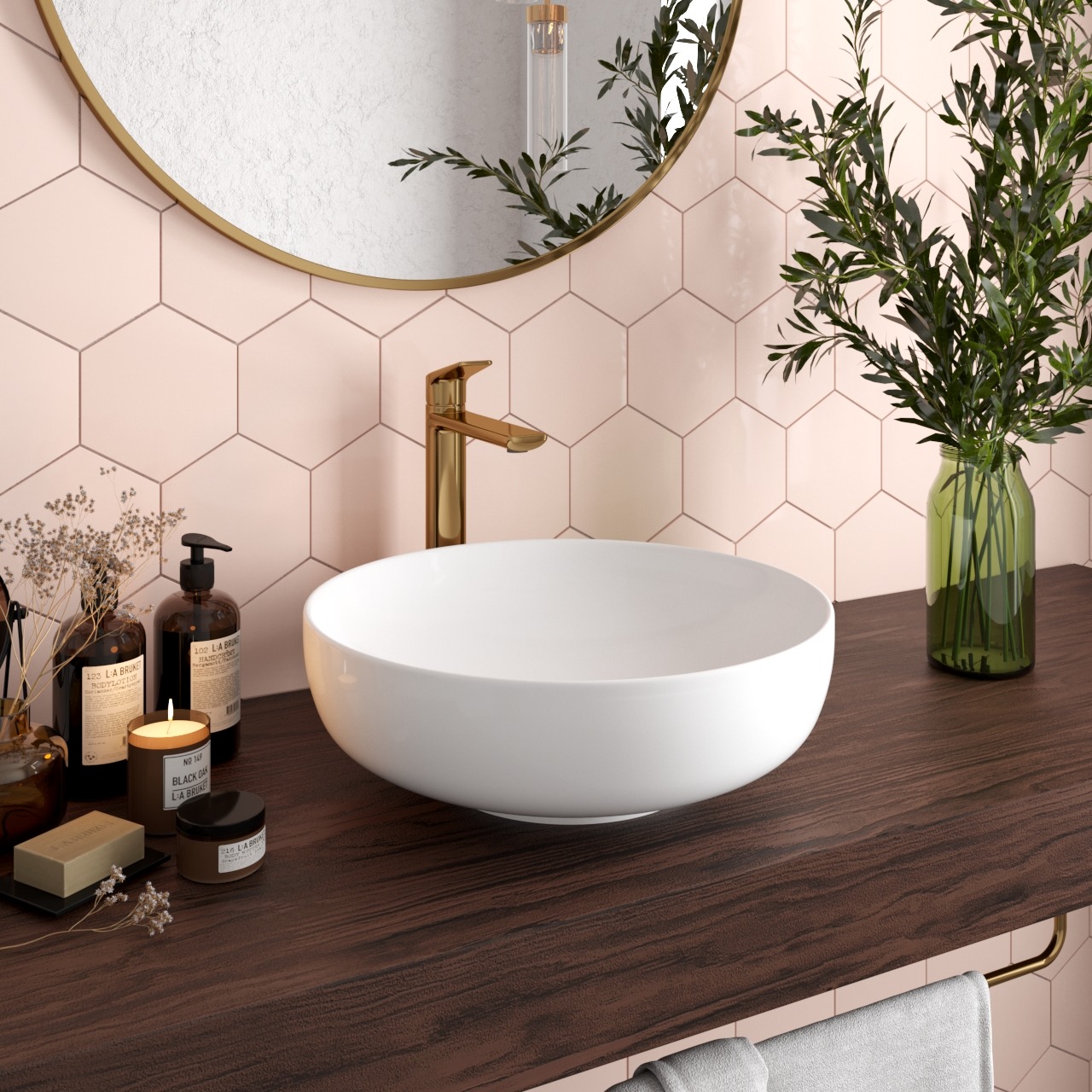 Nowoczesna łazienka z okrągłym lustrem, złotą armaturą i heksagonalnymi płytkami w odcieniach różu. Biała umywalka nablatowa i drewniany blat dodają elegancji.