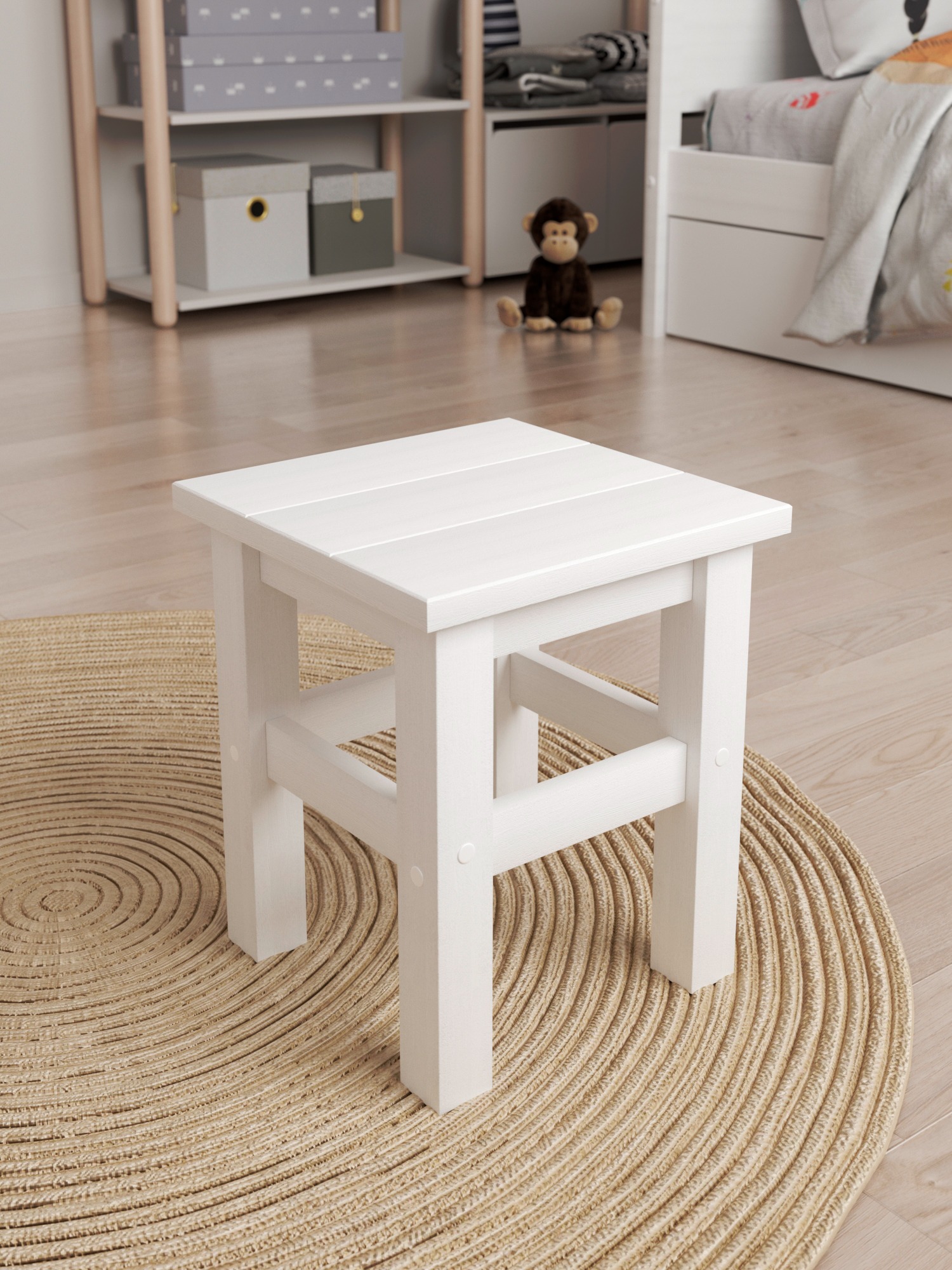 Biały, drewniany taboret na okrągłym, jutowym dywanie w pokoju dziecięcym. W tle regał z pudełkami i łóżko z pluszową małpką. Jasne, naturalne światło.