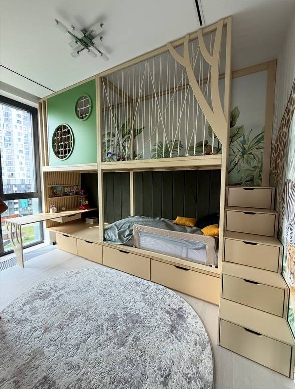 Pokój dziecięcy z łóżkiem na antresoli, biurkiem i schodami z szufladami. Motyw dżungli, okrągły dywan i okna z widokiem na miasto.