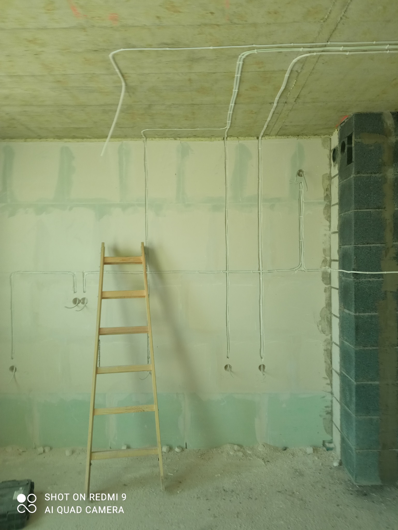 Wnętrze w trakcie remontu z widoczną drabiną i poprowadzonymi przewodami elektrycznymi na ścianie i suficie. Widoczne puszki elektryczne.