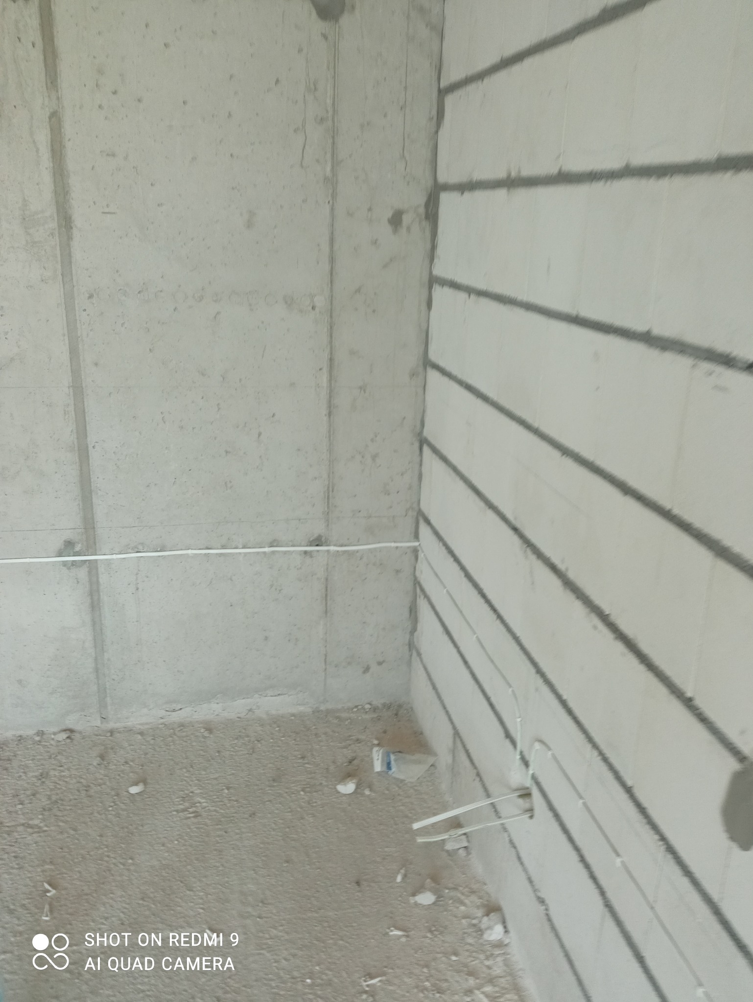 Wnętrze w trakcie prac instalacyjnych: przewody elektryczne prowadzone w ścianie z betonu komórkowego, widoczne bruzdy i fragment podłogi z resztkami materiałów budowlanych.