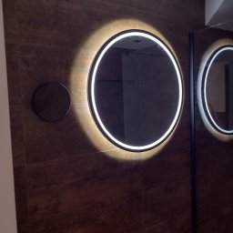 MMJ Marcin Jakubas - Nowoczesna łazienka z dwoma okrągłymi lustrami LED na brązowej ścianie z płytek. Dodatkowe małe okrągłe lustro po lewej stronie. Minimalistyczny design.