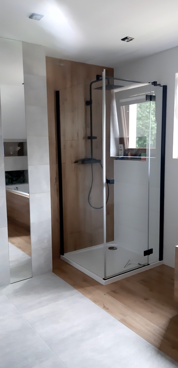 Nowoczesna kabina prysznicowa z czarnymi ramami i deszczownicą w wykończonej łazience w Bielczy. Jasne płytki i drewnopodobne panele tworzą elegancki wystrój.