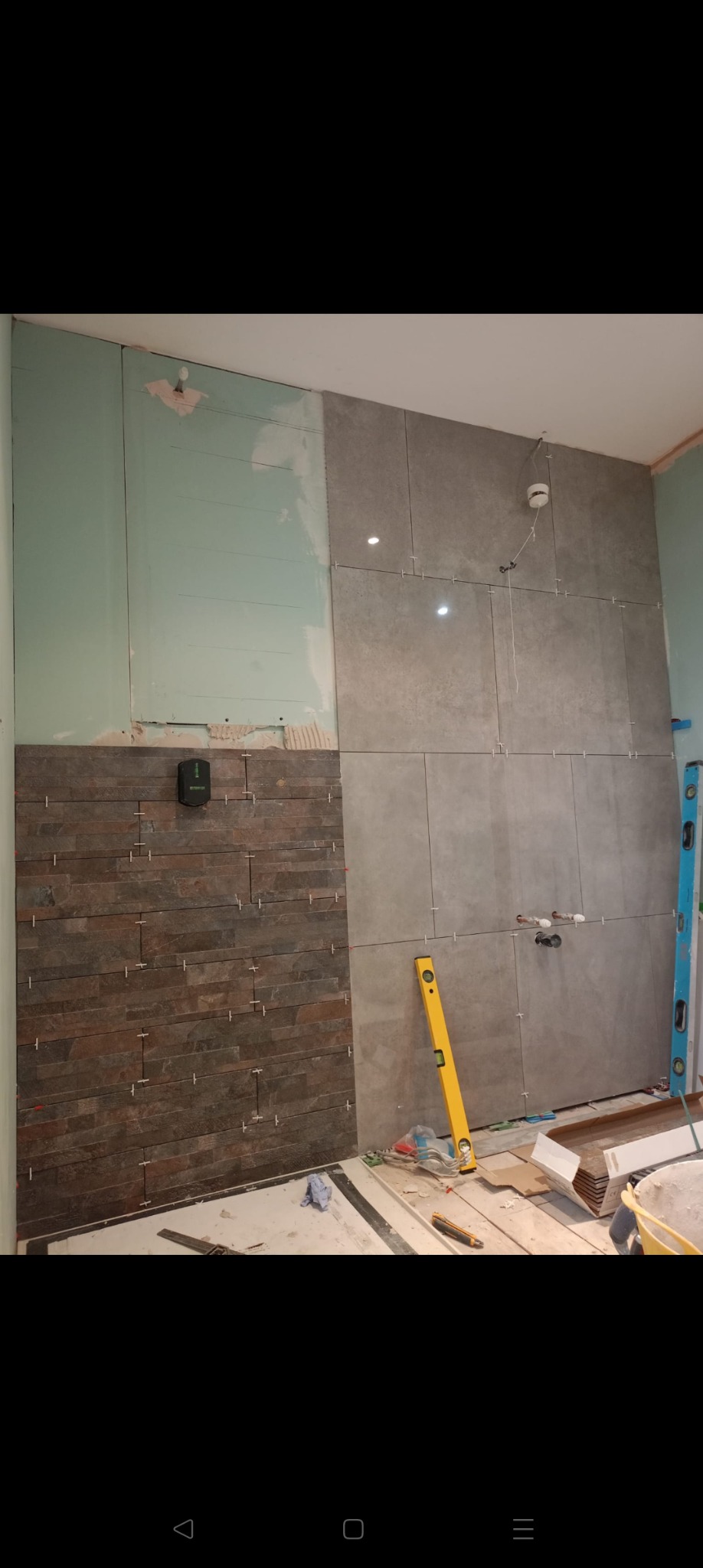 Układanie płytek w łazience: szare płytki wielkoformatowe i dekoracyjne płytki imitujące kamień. Widoczny poziomica, laser krzyżowy i krzyżyki dystansowe.