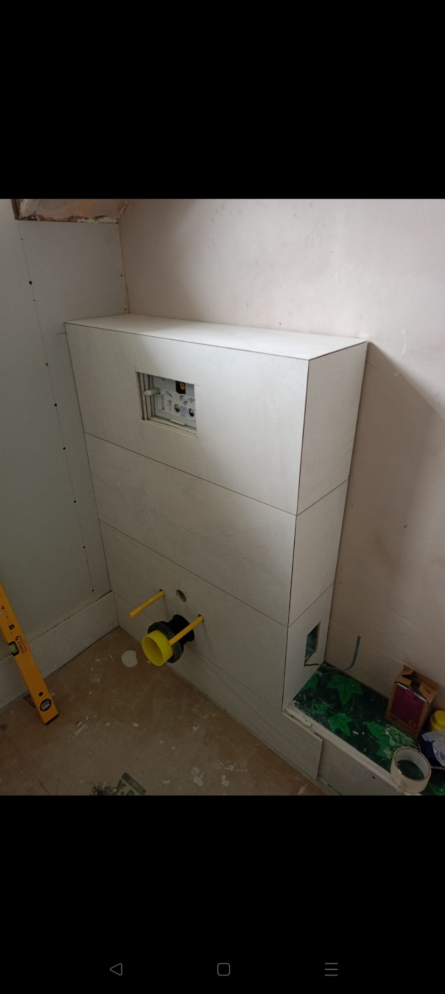 Obudowa stelaża WC z płyt gipsowych w trakcie montażu. Widoczne przyłącza i otwór rewizyjny. Poziomica na podłodze. Prace wykończeniowe w łazience.