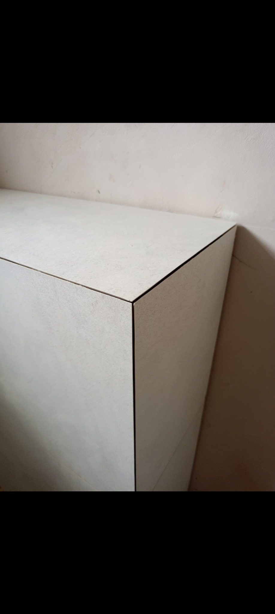 Minimalistyczna zabudowa z jasnych płyt, z widocznymi krawędziami i subtelną fakturą, przylegająca do ściany. Ujęcie z bliska, akcentujące precyzję wykonania.