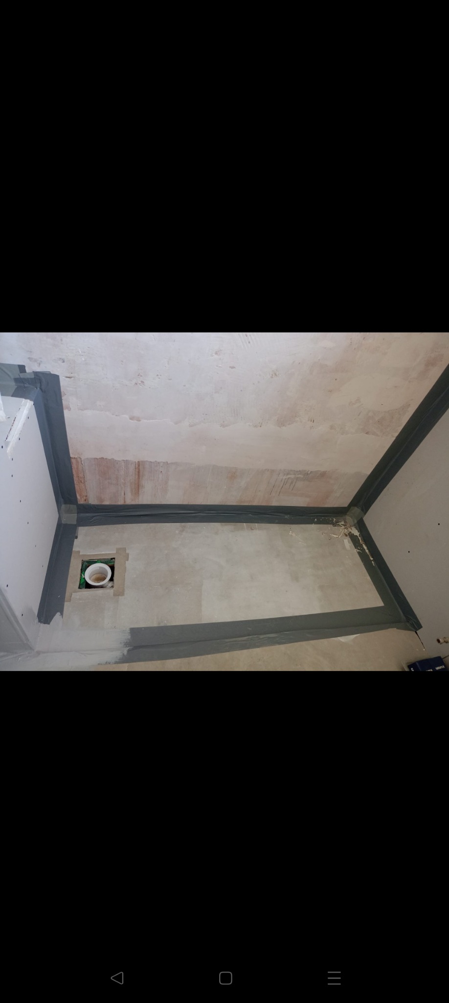 Przygotowana do hydroizolacji podłoga łazienki z odpływem liniowym. Zabezpieczone folią w płynie narożniki i krawędzie. Widoczne ślady po starej posadzce.