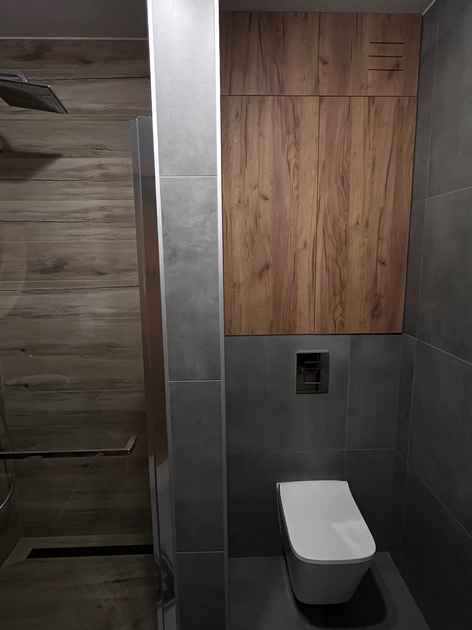 Nowoczesna łazienka w Gdańsku: drewnopodobne płytki, szara armatura i zabudowa nad toaletą. Minimalistyczny design z akcentem naturalnego drewna.