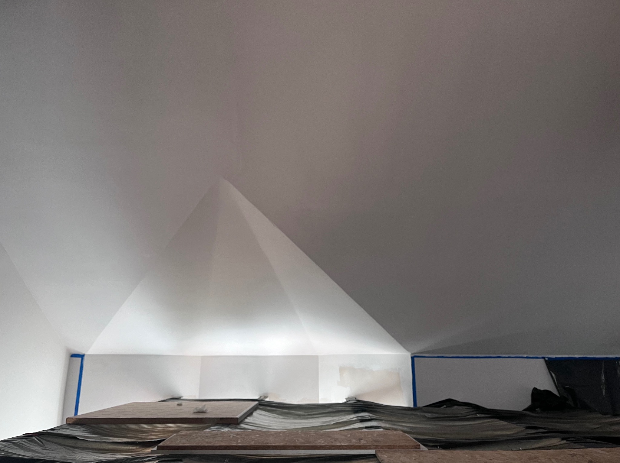 Poddasze po szpachlowaniu, przygotowane do malowania. Widoczne zabezpieczenia folią i taśmą malarską. Świeżo wyszpachlowana ściana pod skosem.