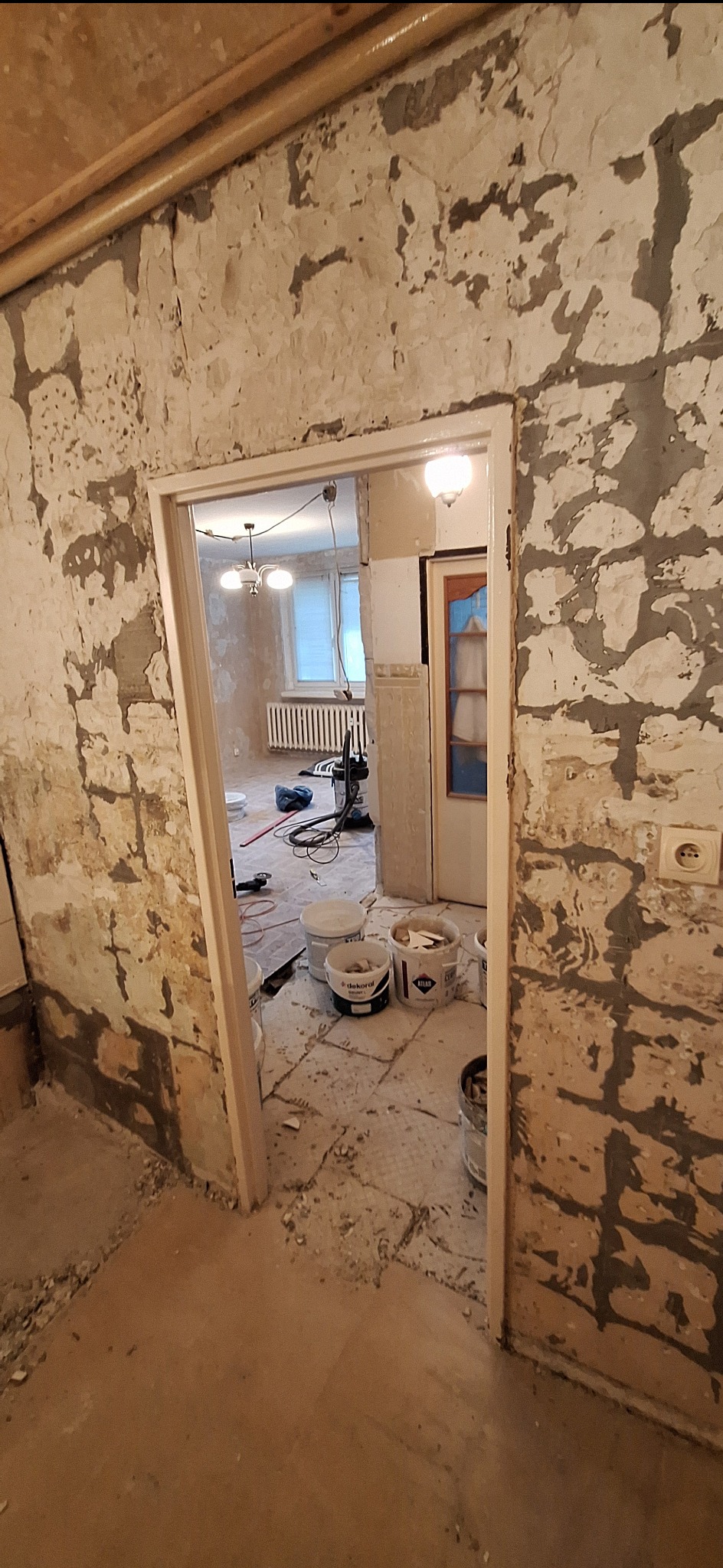 Wnętrze w trakcie remontu: ściany z resztkami starej farby i zaprawy, widoczne wiadra z farbą i narzędzia, przygotowanie do szpachlowania i malowania.