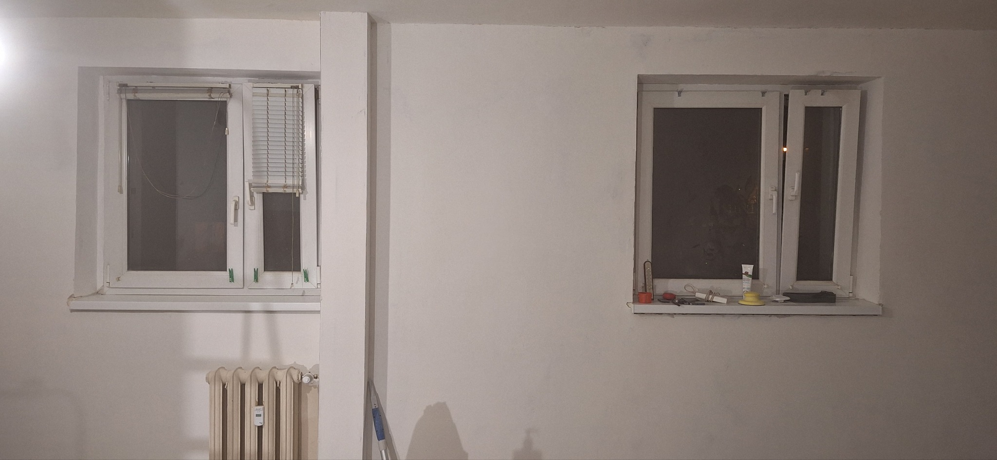 Białe ściany przed malowaniem z dwoma oknami i grzejnikiem w Gnieźnie. Widoczne niedoskonałości i przygotowania do prac malarskich.