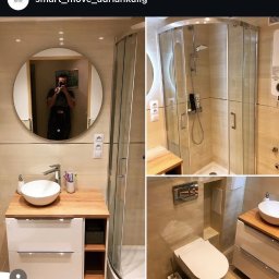 Smart Move Adrian Kulig - Jasna łazienka po remoncie: kabina prysznicowa, umywalka nablatowa na szafce z drewnianym blatem, okrągłe lustro z odbiciem osoby robiącej zdjęcie.