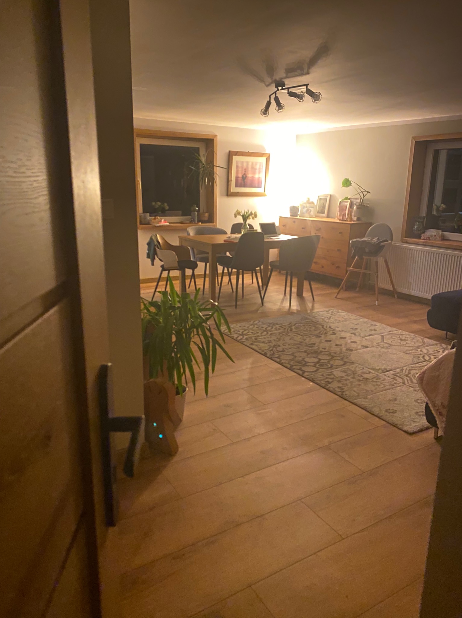 Jasne, przytulne wnętrze jadalni w Wiśle z drewnianą podłogą i stołem. Widok zza otwartych drzwi, z rośliną doniczkową w kadrze. Ciepłe oświetlenie.