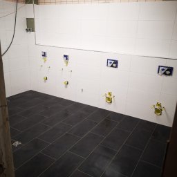 RO-BO-BUD Robert Grzyb - Wykończona łazienka z czarną podłogą z płytek i białymi płytkami na ścianach. Widoczne elementy instalacji sanitarnej. Minimalistyczny design.