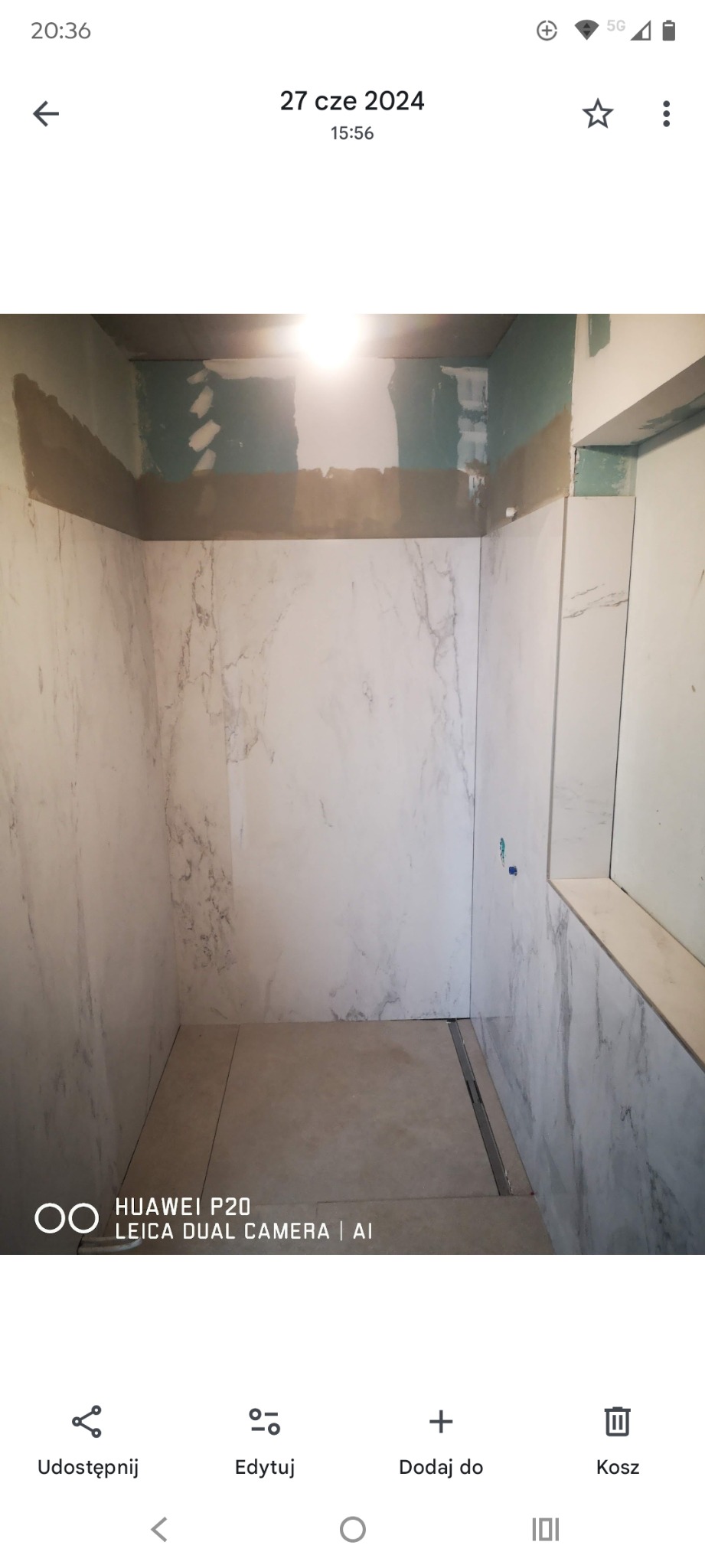 Wykończona łazienka z marmurowymi płytkami na ścianach i beżowymi na podłodze. Widoczny odpływ liniowy. Górna część ścian przygotowana do dalszych prac.