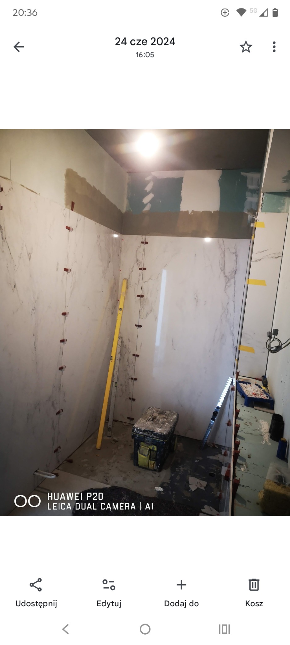 Układanie płytek imitujących marmur w łazience, widoczne poziomica, skrzynka narzędziowa i system poziomowania płytek. Prace glazurnicze w toku.