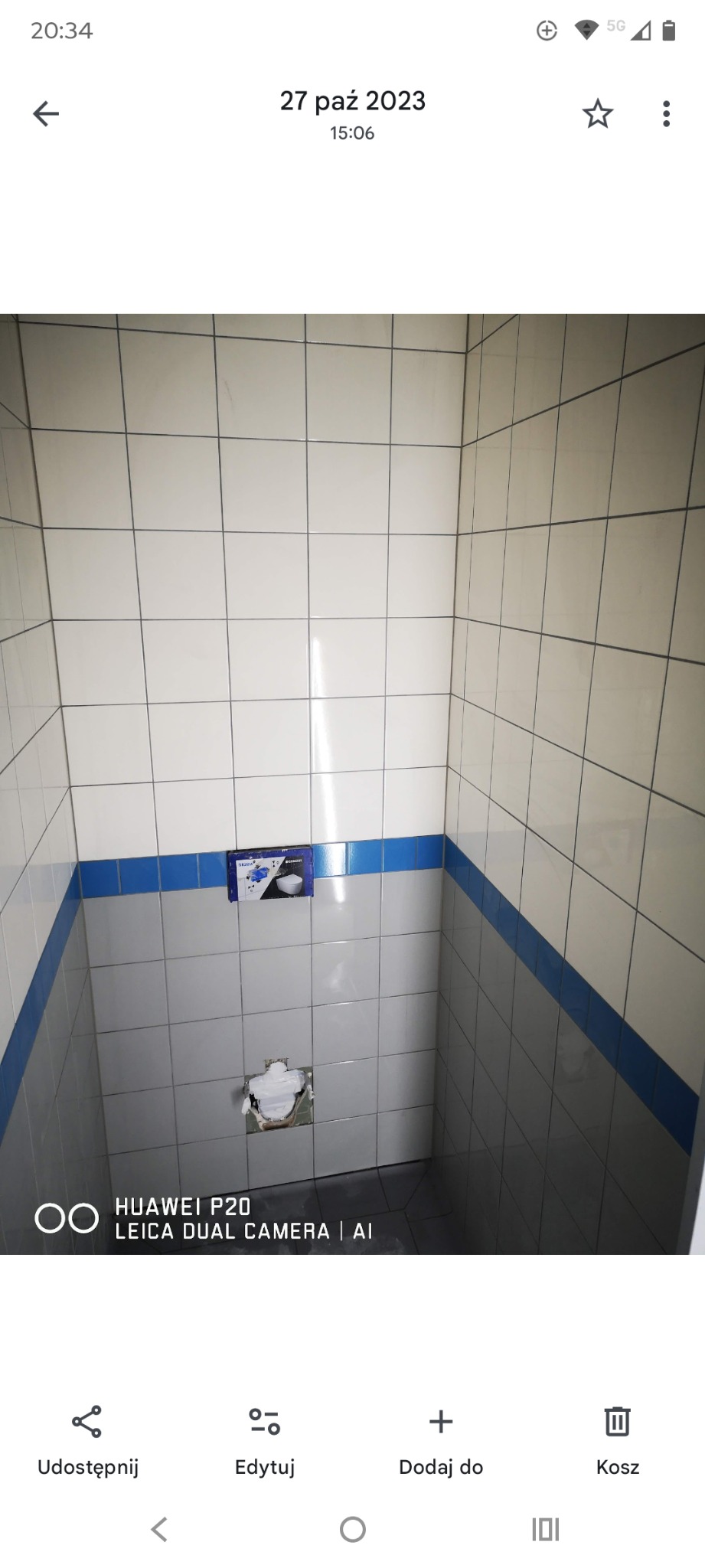 Wnętrze łazienki w trakcie remontu. Widoczne białe płytki z niebieskim pasem, zamontowany stelaż podtynkowy WC i otwór w ścianie po instalacji. Ujęcie z dołu.