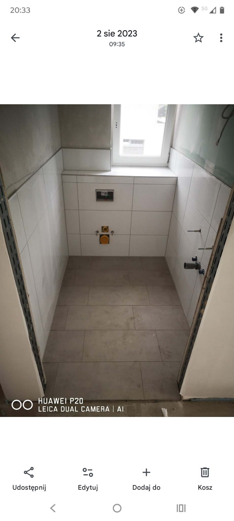 Wykończona łazienka z białymi płytkami ściennymi i szarymi podłogowymi. Widoczne elementy instalacji podtynkowej. Ujęcie z dołu, podkreślające przestrzeń.