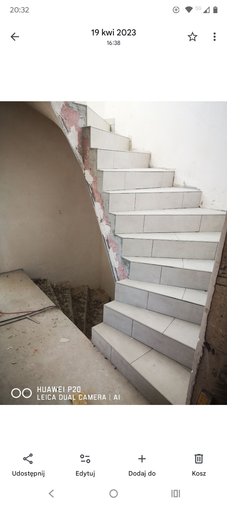 Wykończone płytkami schody wewnątrz budynku, widoczne ślady prac remontowych na ścianach. Jasne płytki, surowy stan otoczenia. Ujęcie z dołu, podkreślające schody.