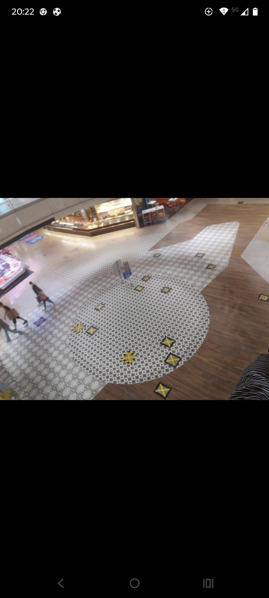 Wnętrze galerii handlowej z nową, wzorzystą posadzką z płytek w odcieniach szarości i brązu. Widoczne oznaczenia dystansu społecznego i fragmenty sklepów.