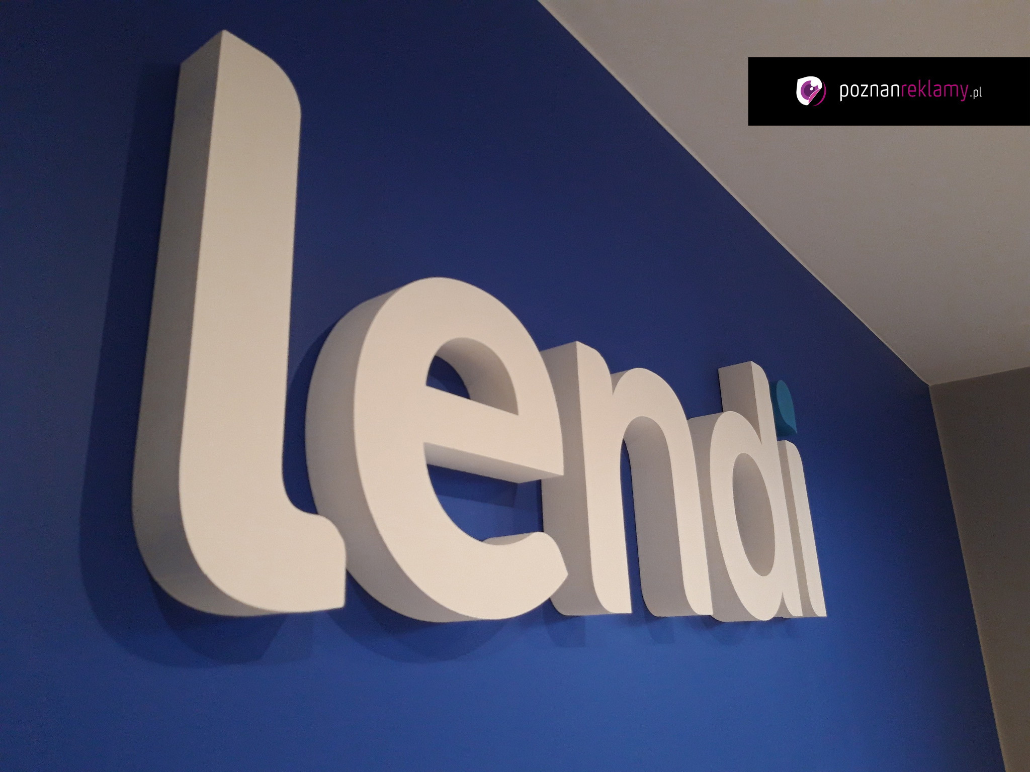 Białe, przestrzenne litery 3D układające się w napis 'Lendi' na intensywnie niebieskiej ścianie. Widoczny fragment logo firmy w prawym górnym rogu.