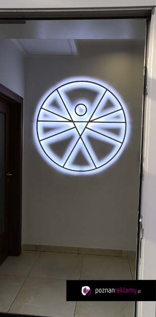 Podświetlane logo firmy w kształcie okręgu z wpisanymi trójkątami, umieszczone na ścianie w korytarzu. Nowoczesny design, subtelne oświetlenie.