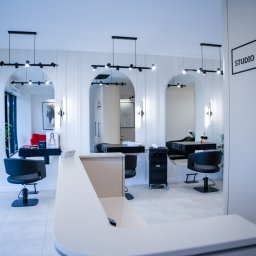 P2Studio Mateusz Grzesik - Nowoczesne wnętrze salonu fryzjerskiego z recepcją, stanowiskami pracy z lustrami w łukowych wnękach, oświetleniem punktowym i rośliną doniczkową przy oknie.
